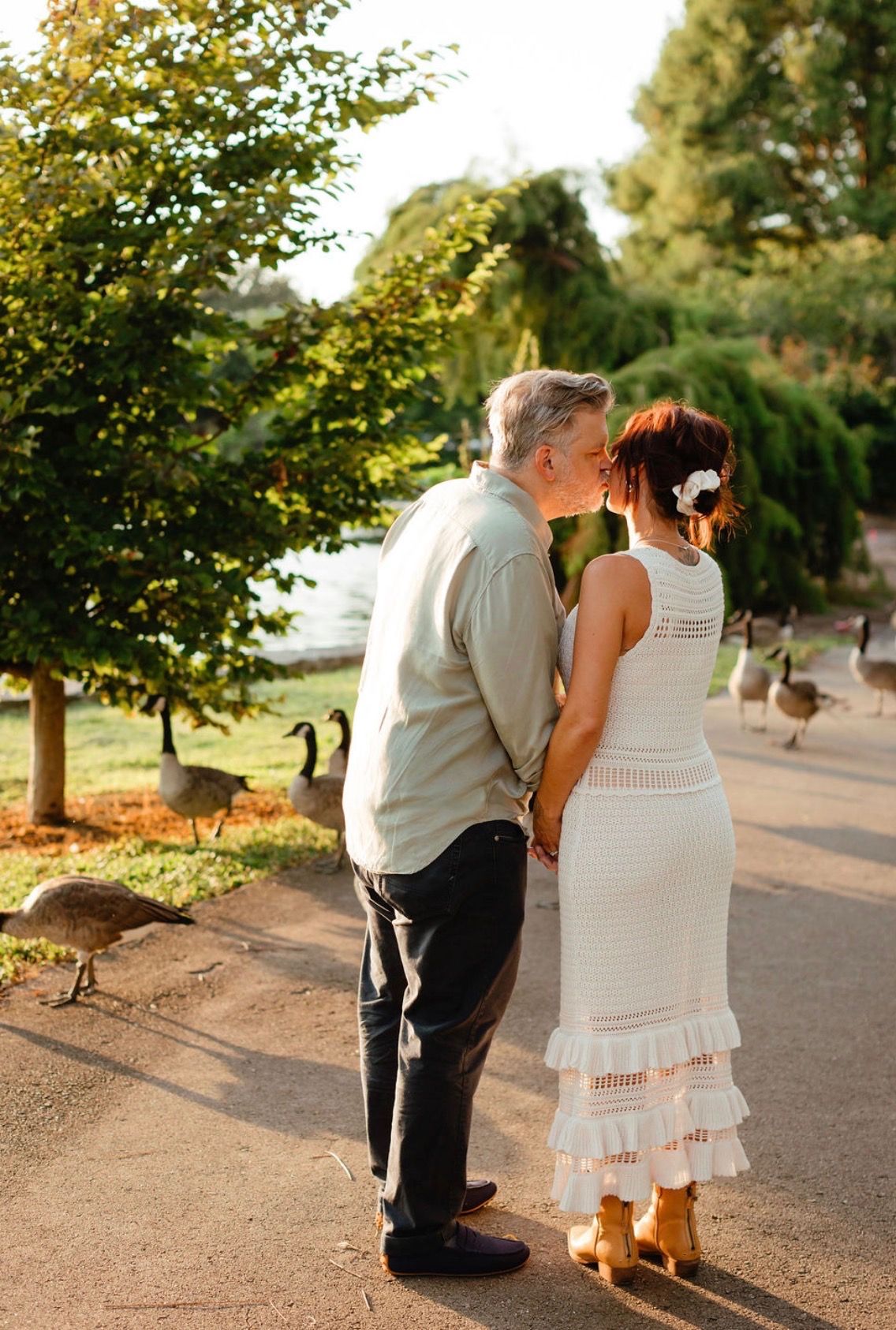 Danielle and Patrick kissing from behind on a path with Canada geese nearby