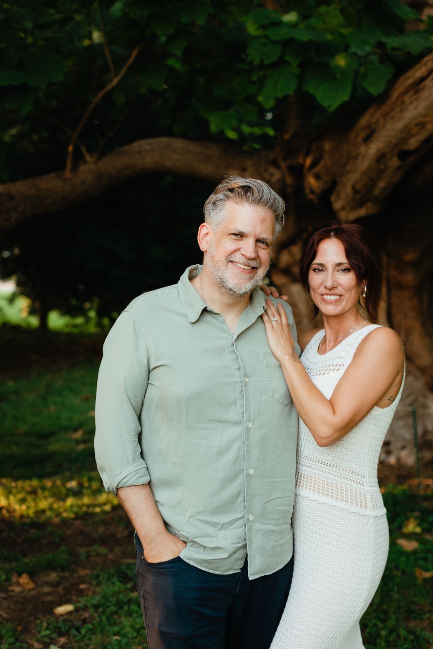 Danielle and Patrick standing together smiling in front of a large tree